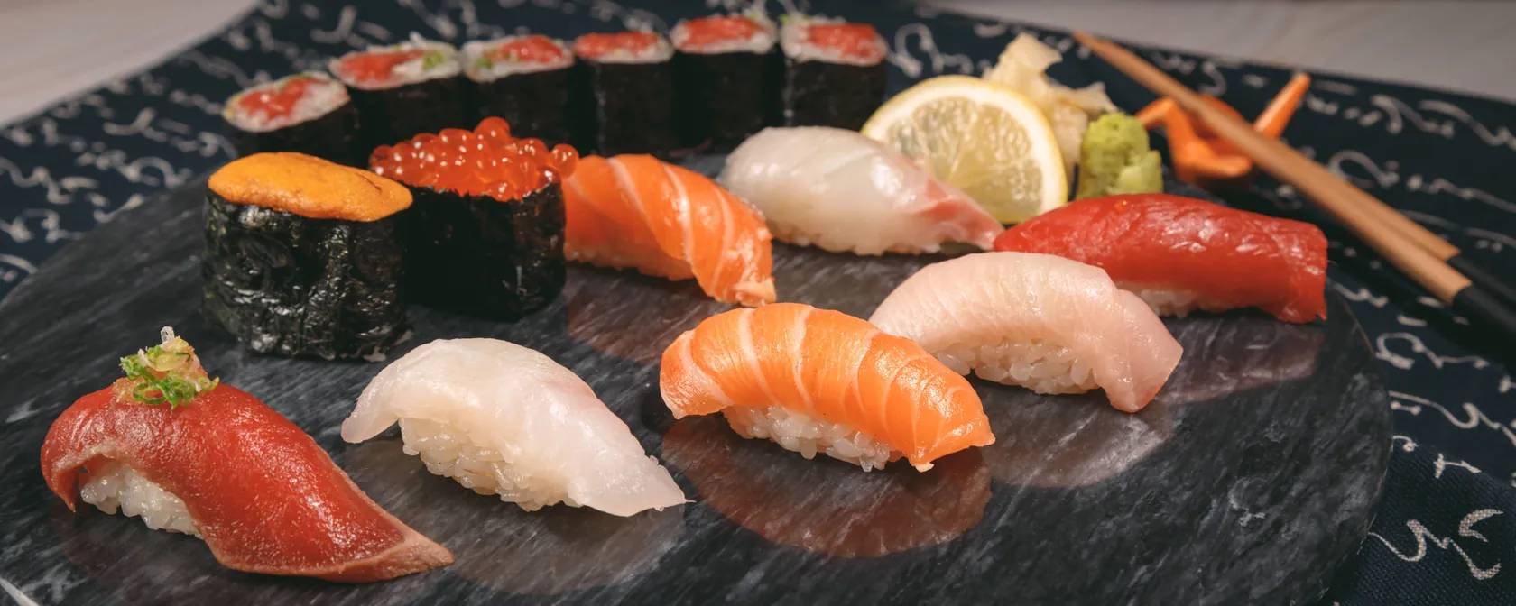 Nigiri of tuna, salmon, yellowtail and white fish, sea urchin and salmon roe, and a tuna roll on a stone plate